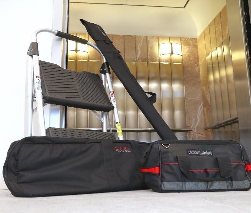 Four-part elevator rescue kit staged at a hoistway: pick bag, equipment-room bag, pole bag, and folding step stool